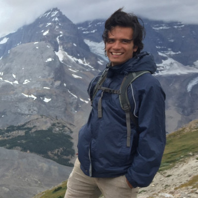 Image shows Erick standing in front of a mountain wearing a navy blue jacket and smiling
