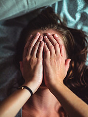 Image shows a woman with her hands covering her entire face