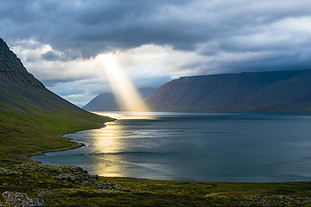 Beam of sunglight falling on a mountain lake through a cloudy sky