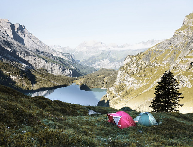 Image shows a mountain vista with a pair of tents, one pink and one blue, set up in the foreground