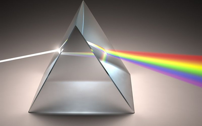 Image shows a prism with a beam of white light entering one side and the spectrum of the rainbow emerging from the other side