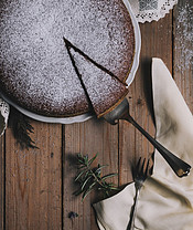Image shows a chocolate cake frosted with frosting sugar with a slice being cut out from it