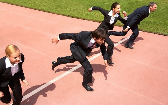 Image shows a group of four people in suits running accross a finish line