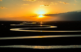 Image shows a winding river flowing off into the distance with the sun positioned above the horizon